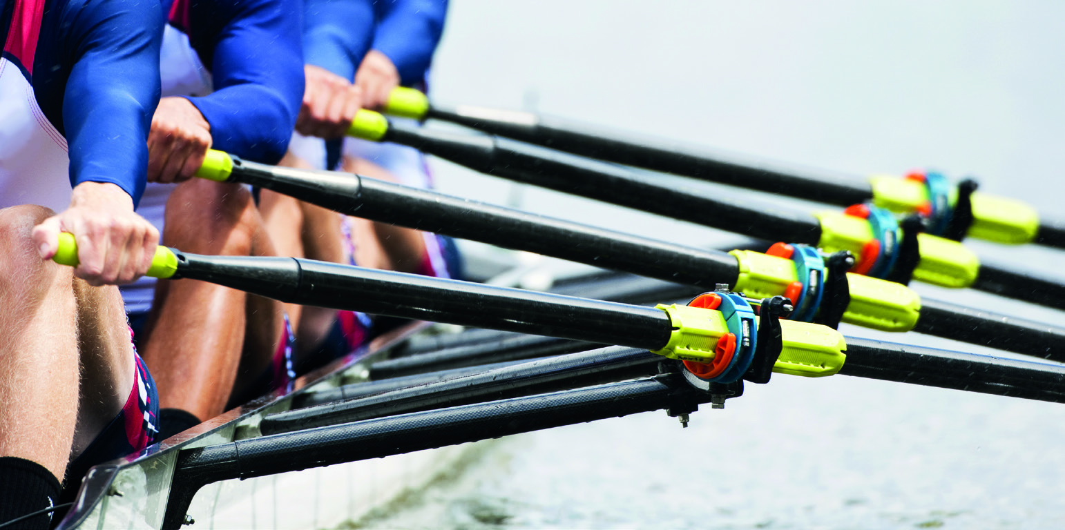 Ruderer in blauer und weißer Sportkleidung rudern synchron in einem Wettkampf auf dem Wasser.